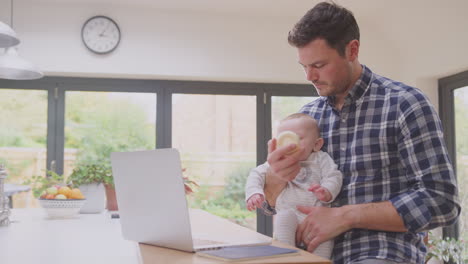 working father using laptop at home whilst feeding baby son sitting on his knee  from bottle - shot in slow motion