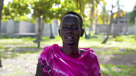 hombre africano masai sonriente vestido de rosa en el palmeral de la aldea