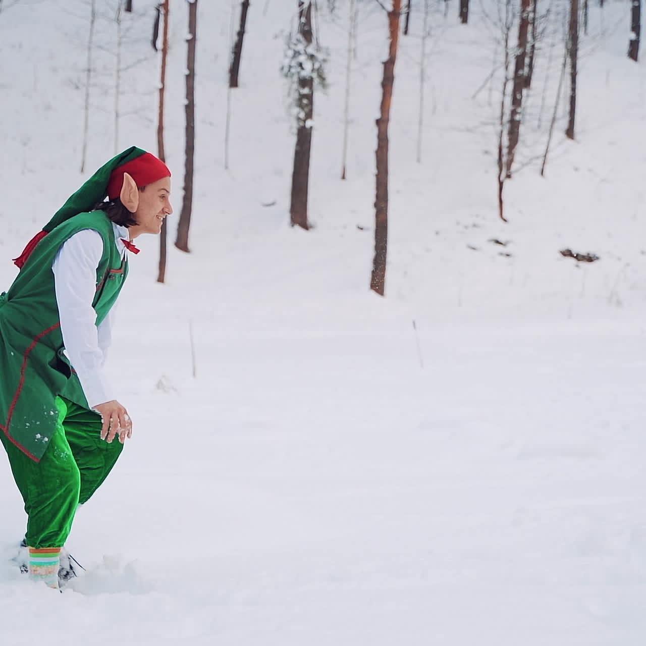Happy elves in green costumes with big ears are playing with white snow in the forest. Christmas characters elves are having fun in the woods in winter outdoors.