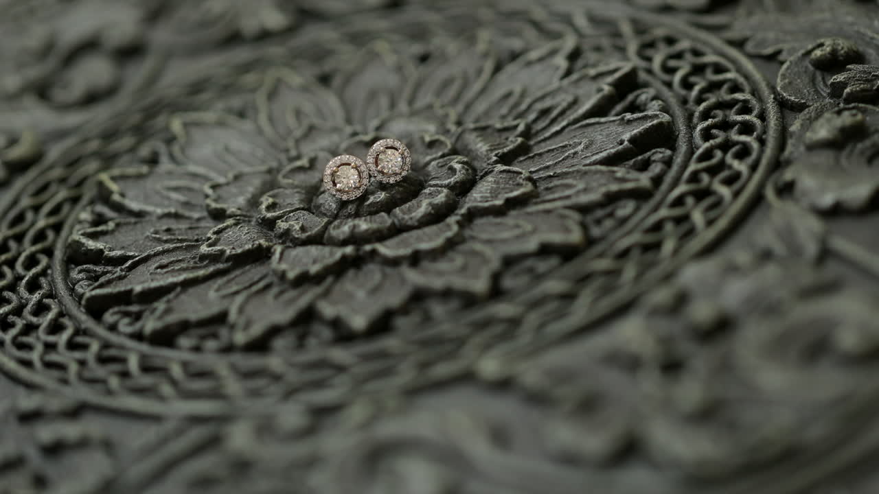 Diamond earrings lying on wood carved with florals, rack focus