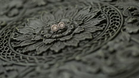 diamond earrings lying on wood carved with florals, rack focus