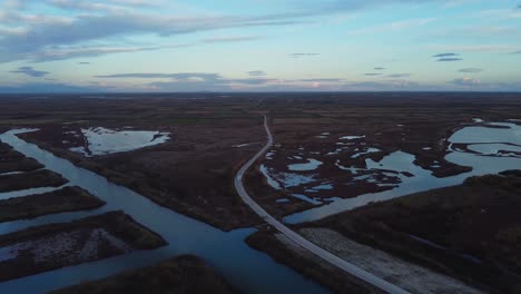 aerial pull back over vast plain and road with fields and lagoons at dusk, greece