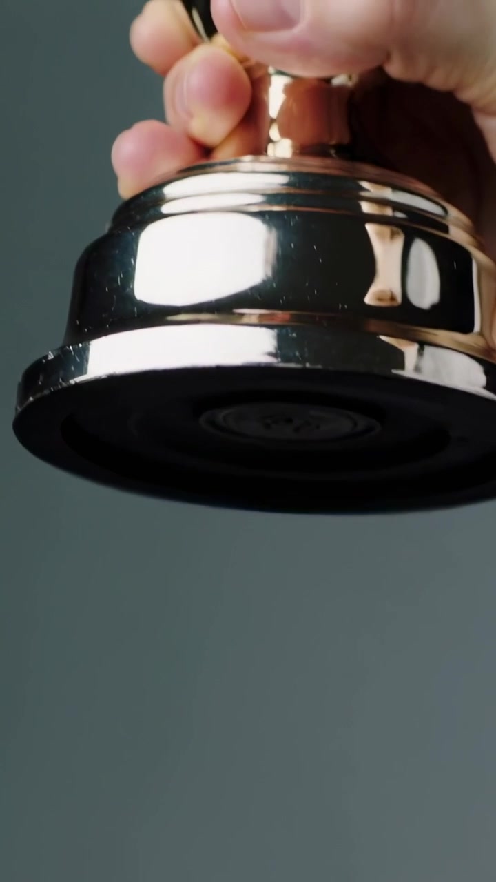 Vídeo vertical: Uma única mão alcançando e girando um troféu brilhante em um fundo cinza, revelando uma base de borracha.