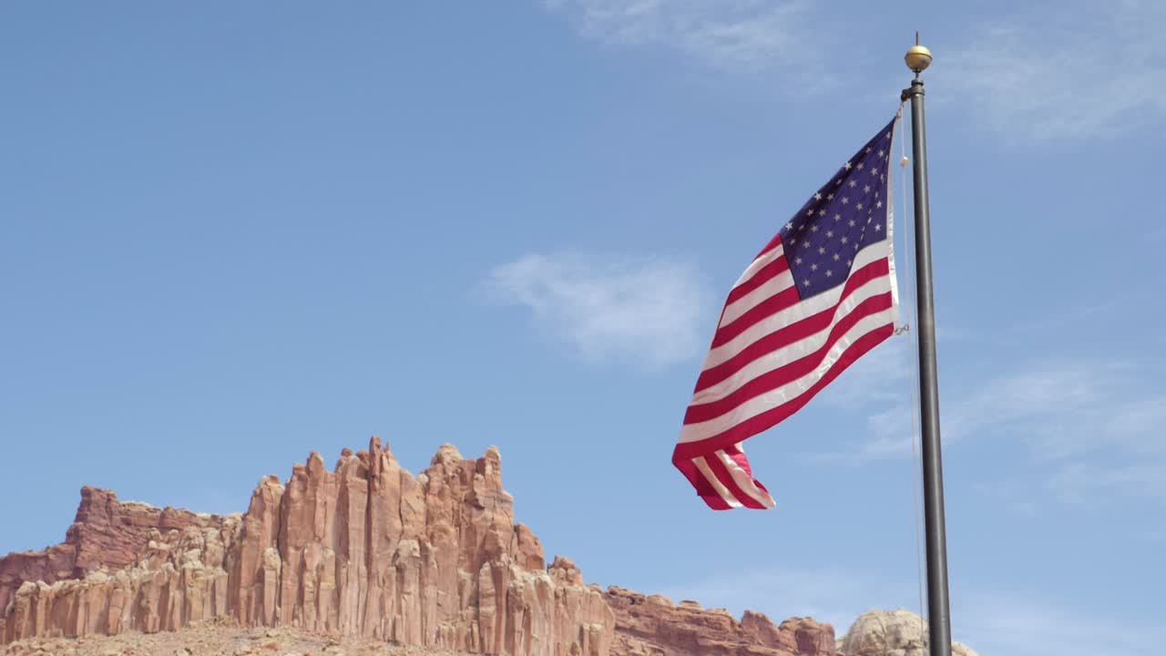 Ripresa al rallentatore della bandiera degli Stati Uniti che sventola al vento davanti a enormi rocce nel Parco Nazionale di Capitol Reef nello Utah, USA
