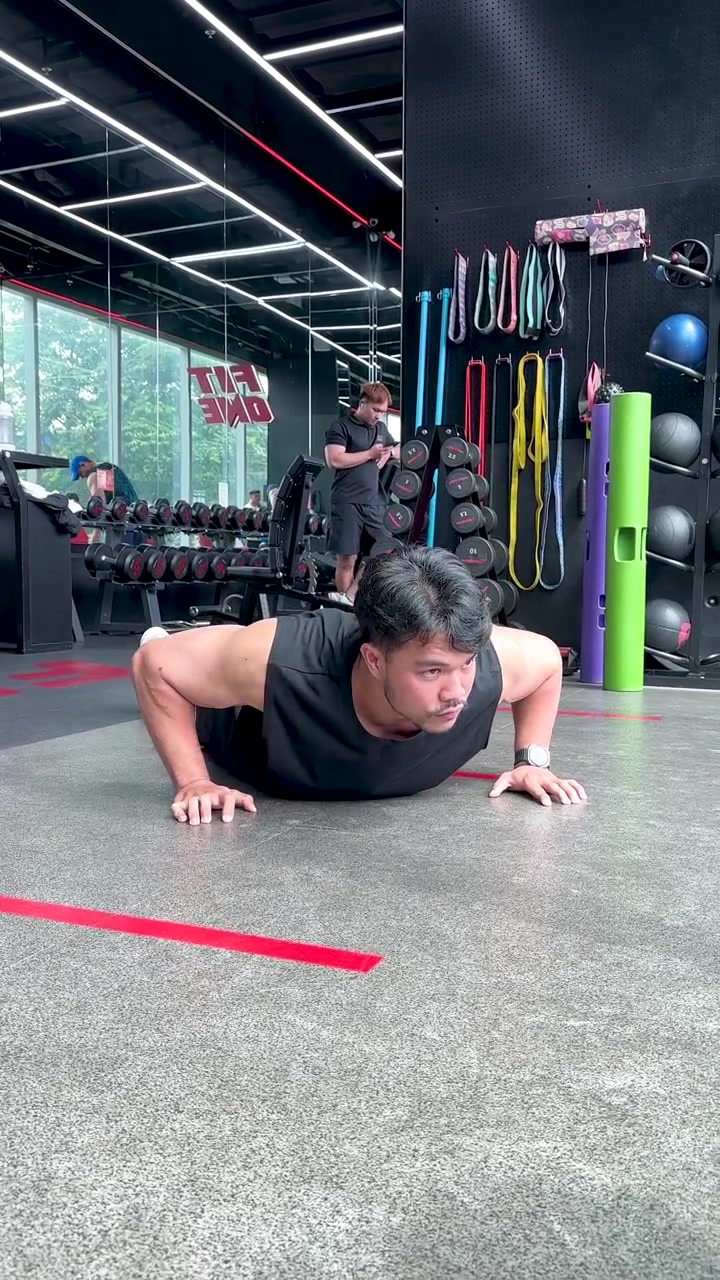 Uomo atletico esegue flessioni sul pavimento della palestra, illuminazione brillante, inquadratura ampia, ambiente incentrato sul fitness.