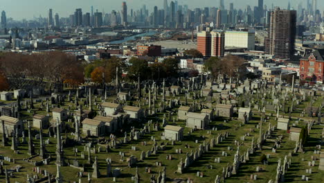 Forwards-fly-above-old-Calvary-Cemetery.-Gravestones-and-tombs-in-green-grass.-Tilt-up-reveal-of-tall-high-rise-buildings.-Queens,-New-York-City,-USA