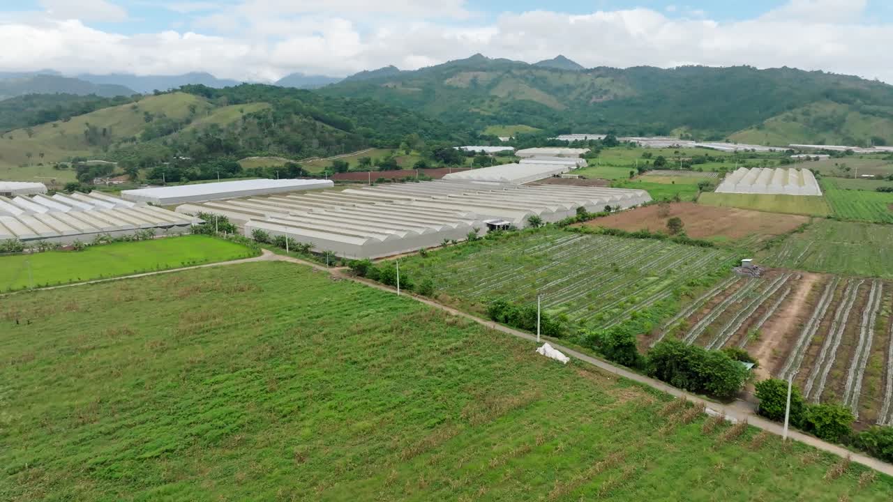 Aerial flyover greenhouses growing vegetables in rural countryside area of Arriba, ocoa, Dominican Republic. Cloudy summer day in suburb