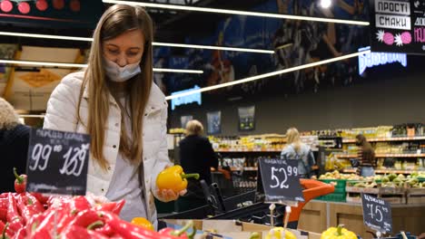 woman hand takes and examines fresh pink tomatoes on branch from display case at vegetable counter in supermarket.