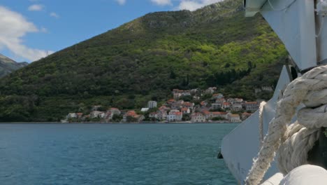 Ferry-arriving-to-a-seaside-village-by-the-mountains,-Adriatic-Sea,-Montenegro