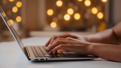 close-up of hands typing on a laptop keyboard with bokeh lights