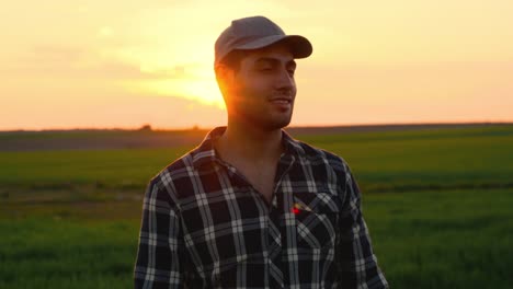 handsome farmer putting on his cap at sunset. positive young farmer looking at agricultural field during scenic sunset. high quality 4k footage