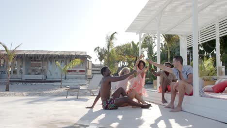 Happy-diverse-group-of-friends-drinking-beer-at-beach-with-beach-house