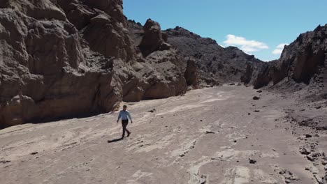 camera rotates to follow woman walking alone in rugged narrow canyon