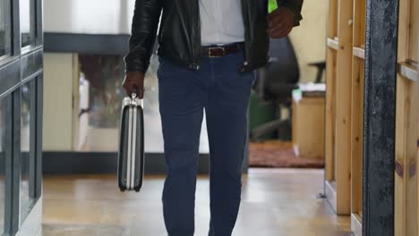 agent man walking with black briefcase in hand wearing leather jacket and jeans. business transaction or travel for secret deal in corporate office. mysterious negotiation or undercover deal operation