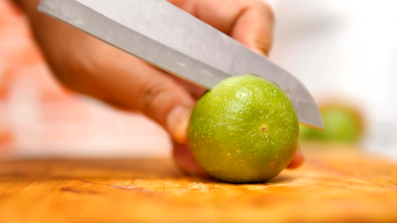 manos de mujeres usando un cuchillo cortando la mitad de la cal verde en una tabla de madera en una cocina