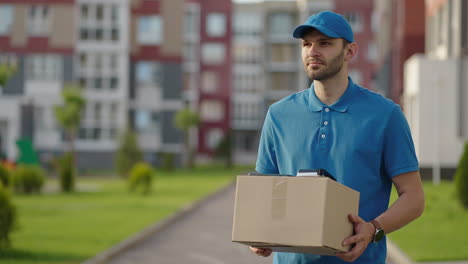 Blue-delivery-man-send-a-package-to-customer-on-before-deliver-cargo.-4k-resolution-and-slow-motion-shot.-Male-postman-with-parcel-in-hands-at-city-street.-Postal-concept.-Delivery-service.