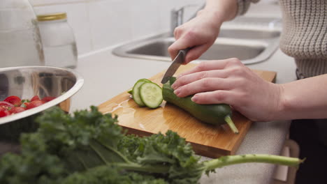 Hands-cutting-cucumber-for-a-salad-with-greens-on-the-foreground