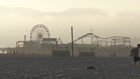 A-Man-Walks-In-The-Sand-In-Front-Of-Santa-Monica-Pier-In-Santa-Monica-California