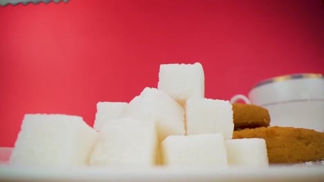 A-close-up-shot-captures-sugar-cubes-being-lifted-with-sugar-tong-and-dropped-into-a-cup-against-a-red-background,-symbolizing-the-concept-of-sweetening-beverages-and-indulging-in-culinary-delights