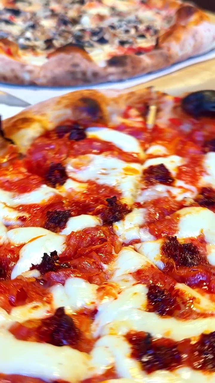 Close-up de duas pessoas segurando pizzas prontas para comer, assadas em forno a lenha, com queijo mussarela derretido, molho de tomate e cobertura de cogumelos.
