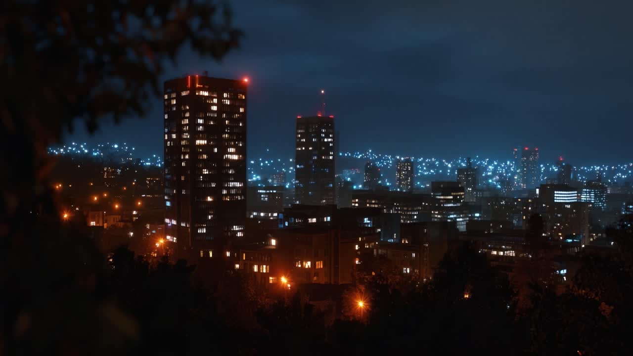 Vista noturna da paisagem urbana a partir de uma encosta. Árvores emolduram a cena, adicionando profundidade. Arranha-céus brilham sob o céu escuro. Luzes da cidade se estendem à distância. Cena urbana perfeita para temas de viagem, urbanos ou noturnos.