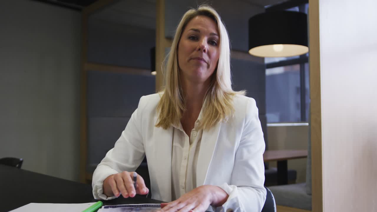 mujer de negocios caucásica teniendo video chat pasando por el papeleo en una oficina moderna