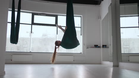 young beautiful woman practice in aero stretching swing. young woman rolls her head upside down in a hammock for aerial yoga. focused pretty mature woman doing aerial yoga in gym