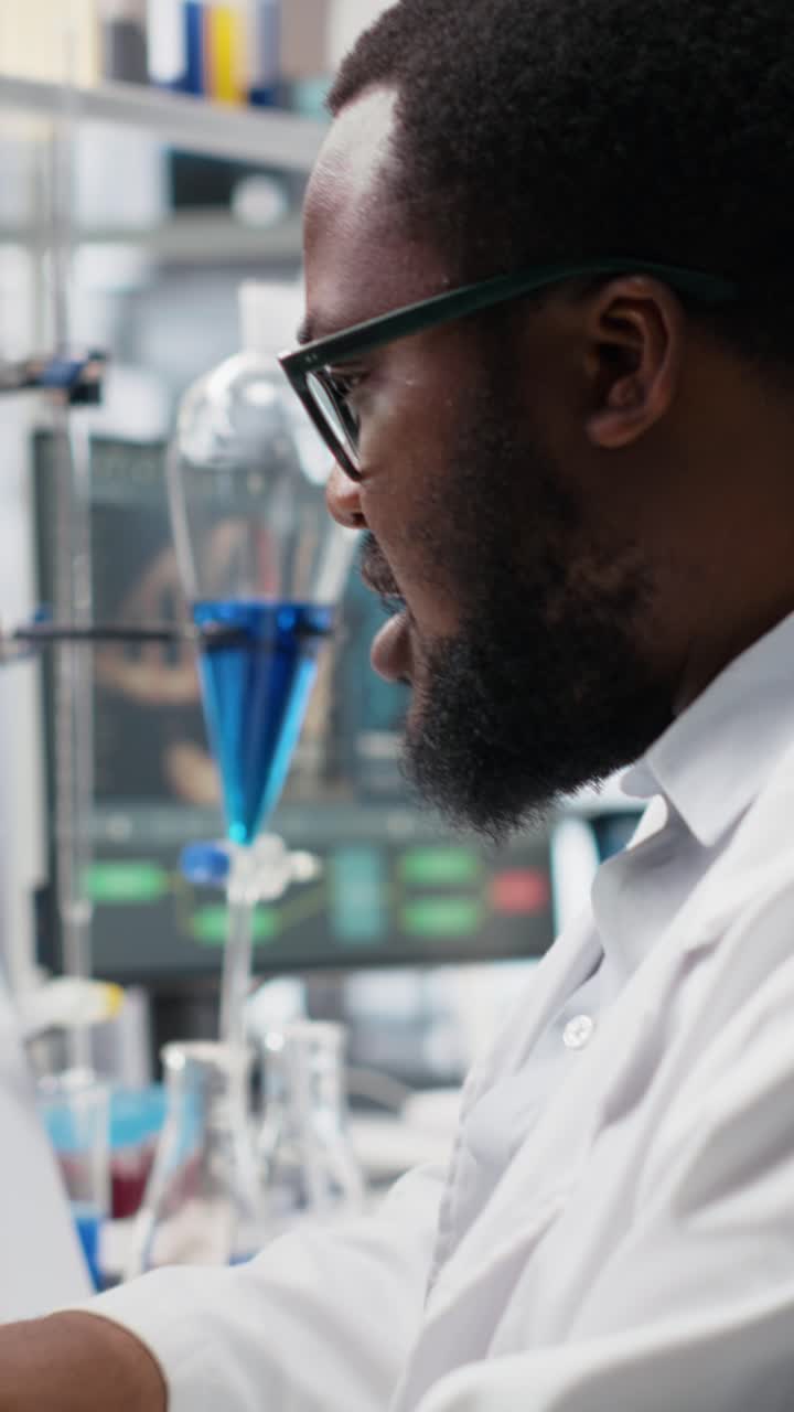 Vidéo verticale : un microbiologiste dans un laboratoire examine une lame à l’aide d’un appareil optique et effectue des analyses sur un PC