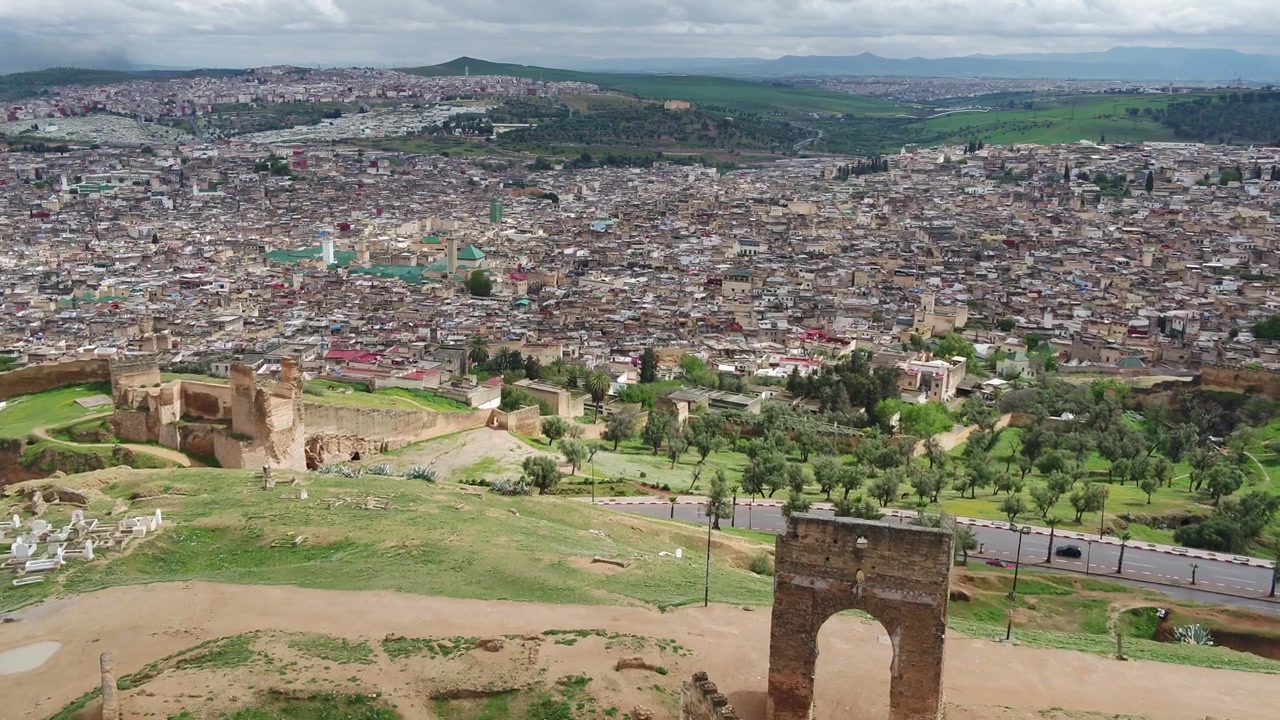 Impresionante vista aérea de dron de las Tumbas Merínidas con vistas a la histórica Medina de Fez, con un amplio paisaje urbano panorámico y colinas verdes en Marruecos, ideal para proyectos de viaje.