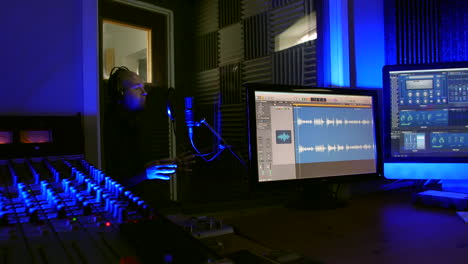 un hombre está grabando una voz en una oscura cabina vocal de un estudio de grabación hablando en un micrófono con un escudo pop