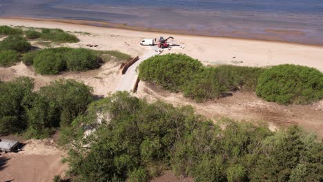 Aerial-view-of-repair-works-along-the-Baltic-Sea-coast,-featuring-visible-construction-machinery-and-a-concrete-footbridge