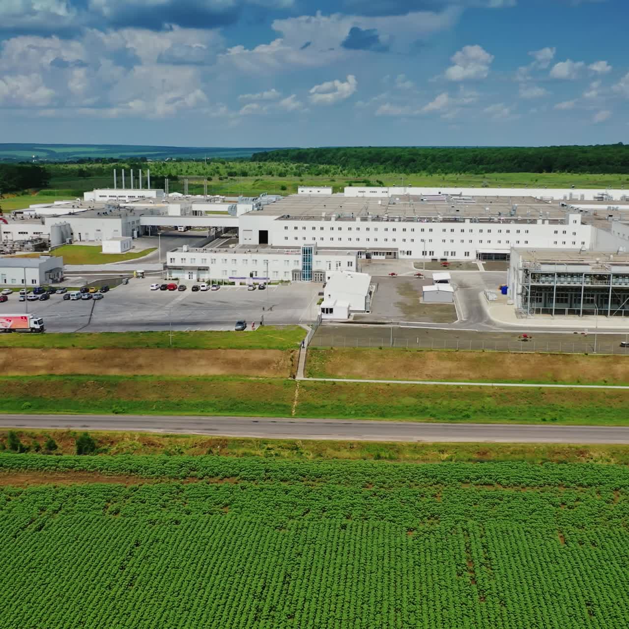 Large industrial plant. Contemporary white buildings of a factory among green fields in summertime. Aerial view. Motion camera to the left.