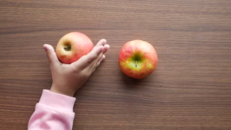 niño sosteniendo y examinando manzanas en una mesa de madera