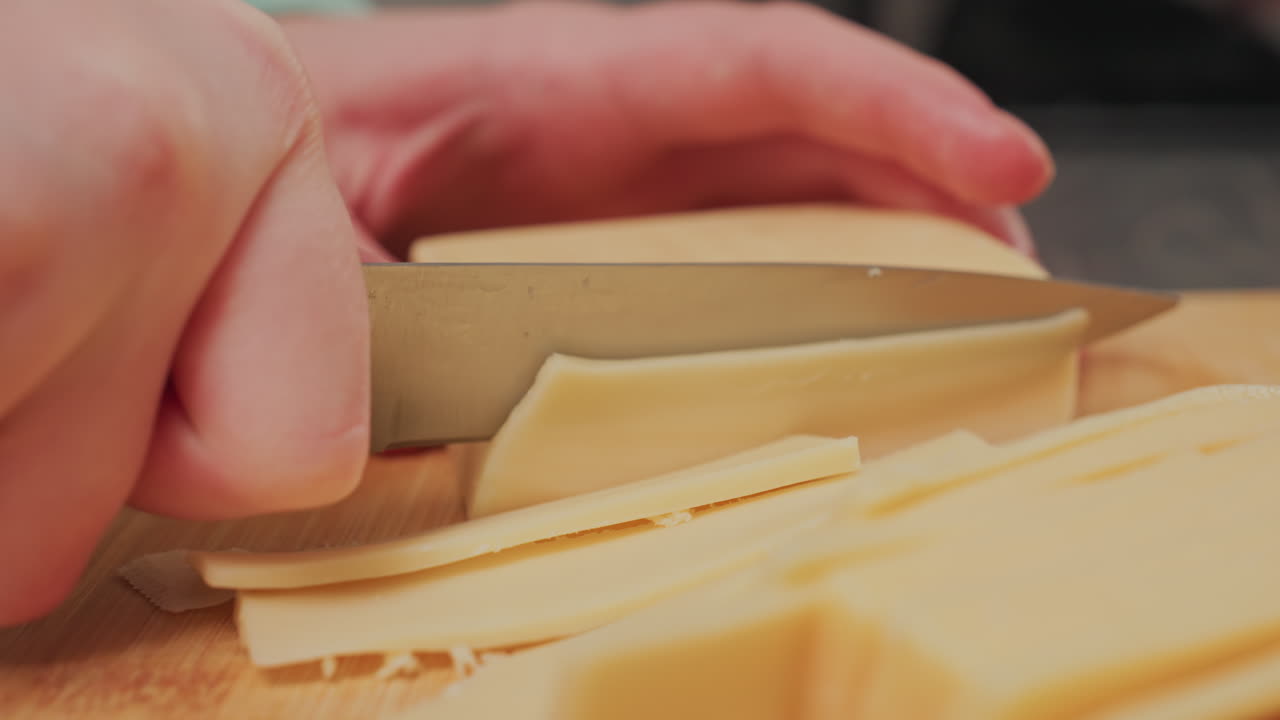 extreme close up of hand slicing through solid block butter with sharp knife on smooth wooden board, showing precise culinary technique during food preparation process in home kitchen