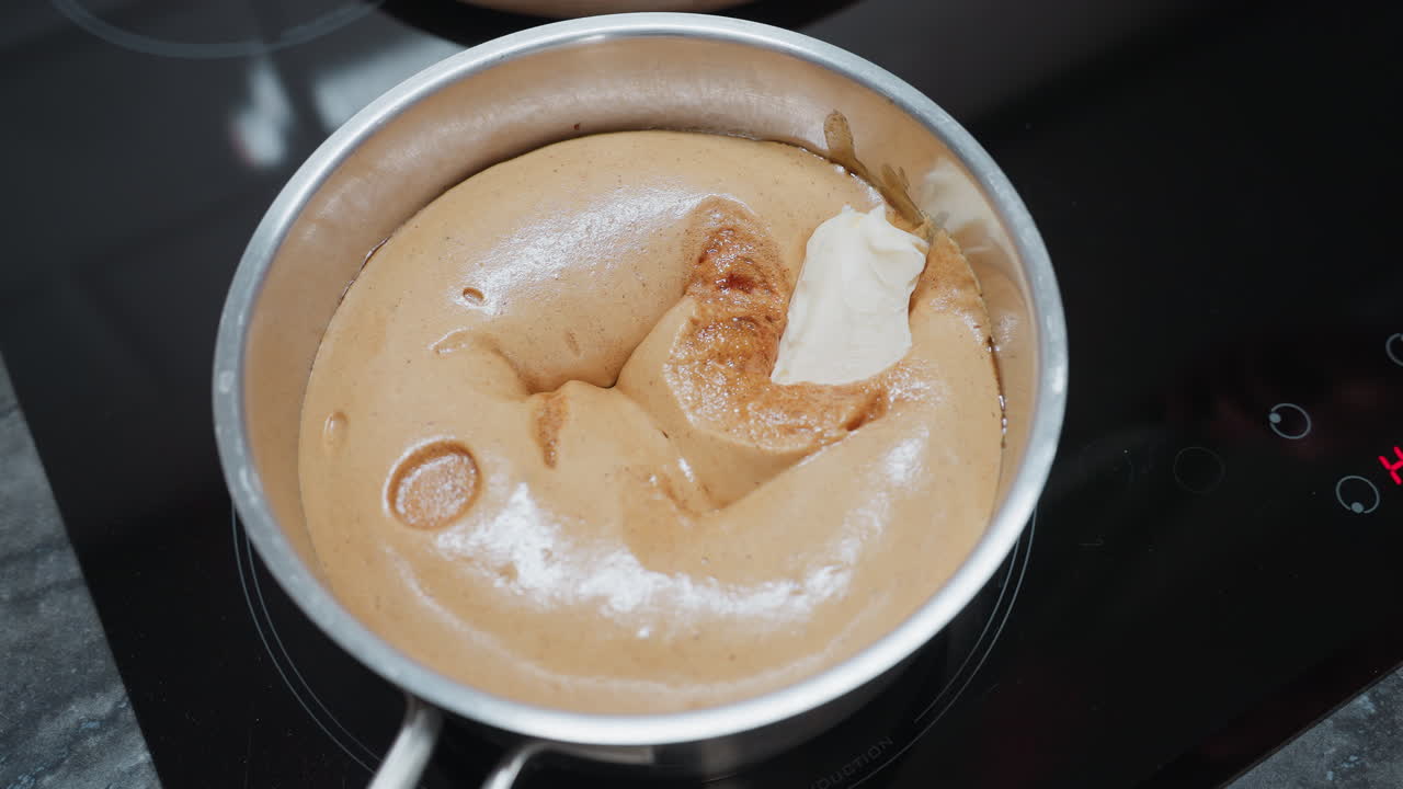 전기 스토브에 마가린을 는 음식에 넣는 사람의 클로즈업, 음식이 두고 거품이 있고, 칼은 혼합물에 녹을 준비가 된 마가린의 어리를 들고 있습니다.