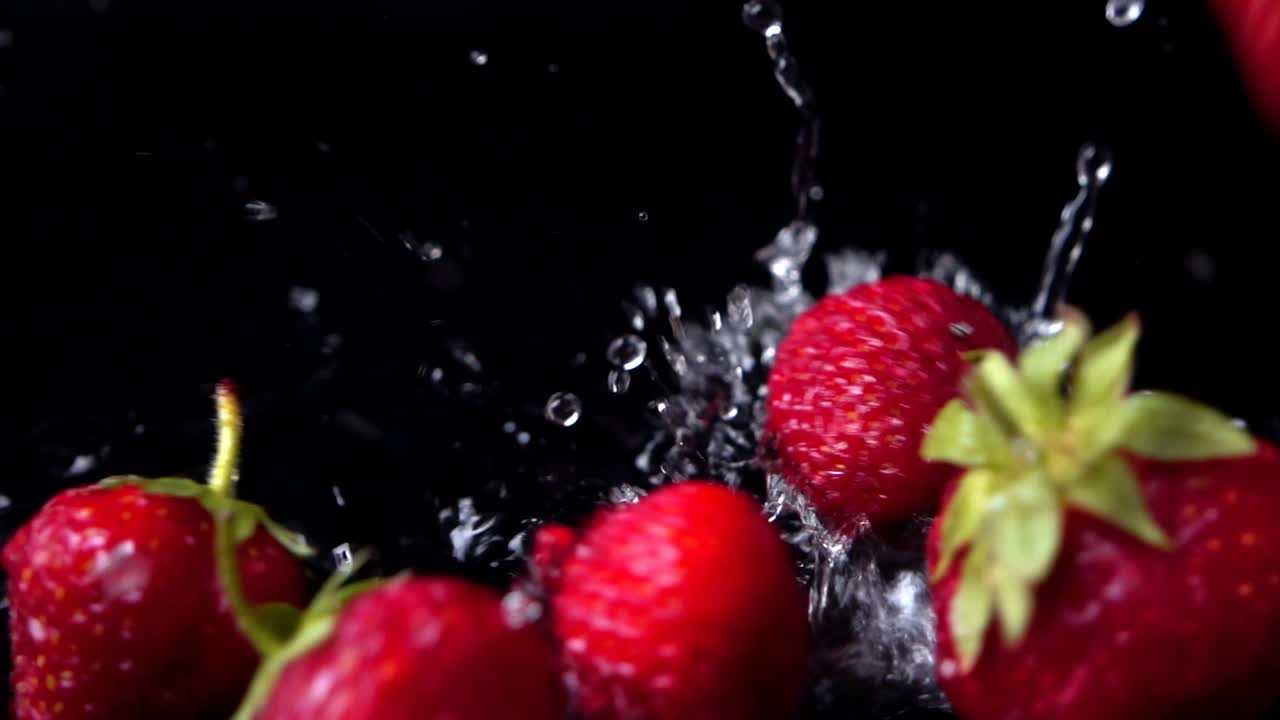Fragola che cade in acqua su sfondo nero. Rallentatore