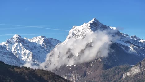 una toma aérea en círculo de un pico de montaña cubierto de nieve escondido detrás de gruesas nubes rodantes