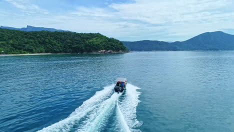 drone follow speedboat cruising on the blue sea leaving foam trails on water surface, mountain range background