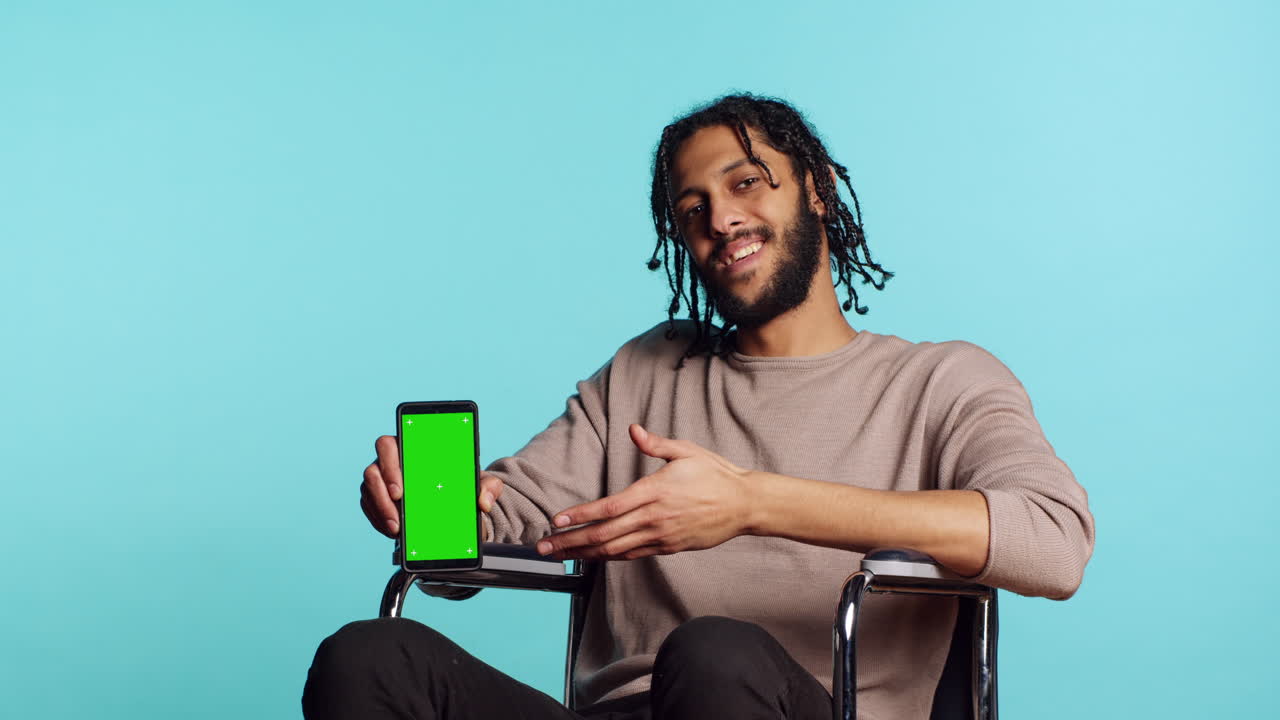 hombre en silla de ruedas apuntando hacia la pantalla verde del teléfono móvil, fondo del estudio
