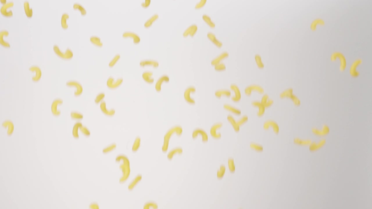 Maccheroni a gomito secchi e crudi che cadono a pioggia su uno sfondo bianco al rallentatore, primo piano macro