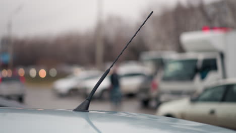 una vista borrosa cercana de automóviles que pasan y otros automóviles estacionados, capturada desde la perspectiva de una antena de automóvil, con luz borrosa vista desde la distancia