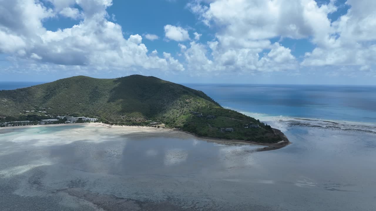 Lenta ripresa con drone di giorno con una leggera panoramica a destra, mantenendo un'ampia vista sul promontorio dell'isola di Hayman, sulle basse acque della baia e sull'oceano aperto, Whitsundays, Queensland, Australia