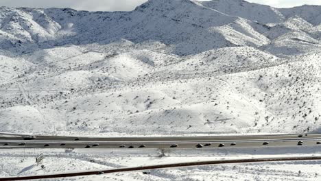 Luftbildverfolgung-Direkt-über-Den-Autobahnverkehr-In-Der-Verschneiten-Berglandschaft-Im-Winter