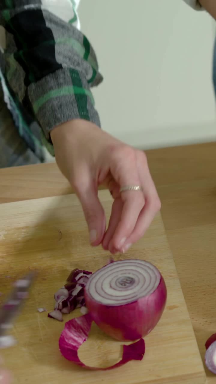 Vertical video: Dicing halved red onion, plaid cook preparing meal on board with knife in kitchen