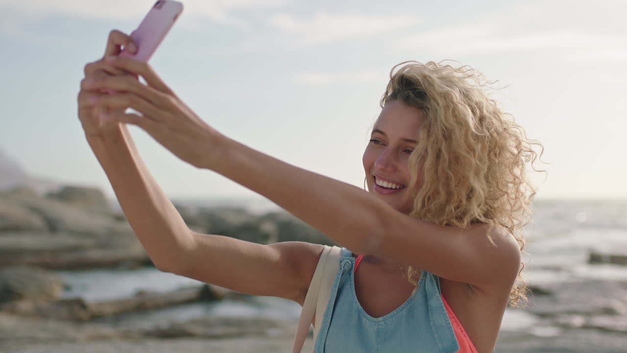retrato de mulher atraente com cabelos encaracolados tirando uma selfie na praia