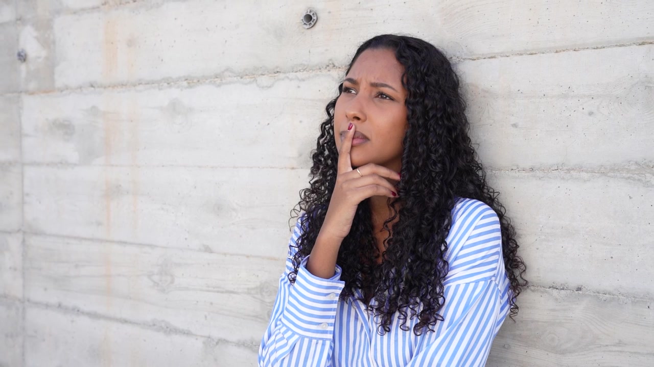 A cheerful smiling woman with beautiful curly hair posing against a rustic concrete wall