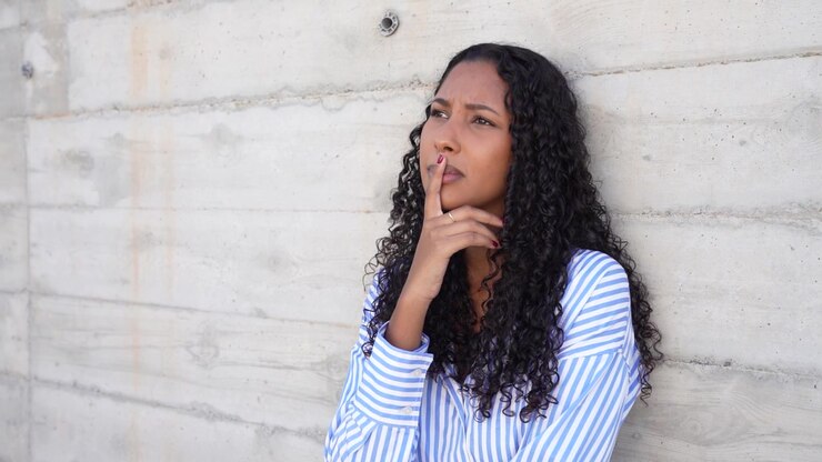 A cheerful smiling woman with beautiful curly hair posing against a rustic concrete wall