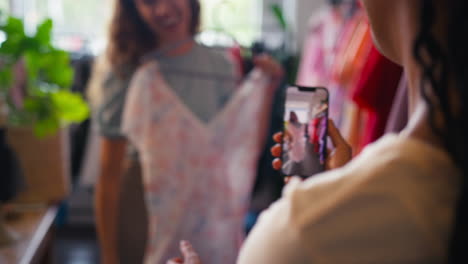 two friends shopping for clothes in fashion store taking video of dress