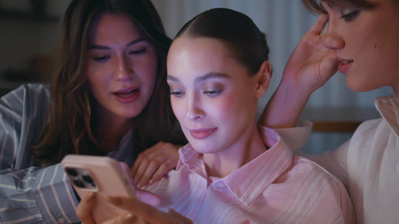 Closeup three women browsing mobile phone social media on evening home couch