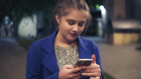 Young-attractive-woman-using-smartphone-at-night-in-city.-Beautiful-girl-texting-on-smartphone-outdoors.-Tourist-Girl-with